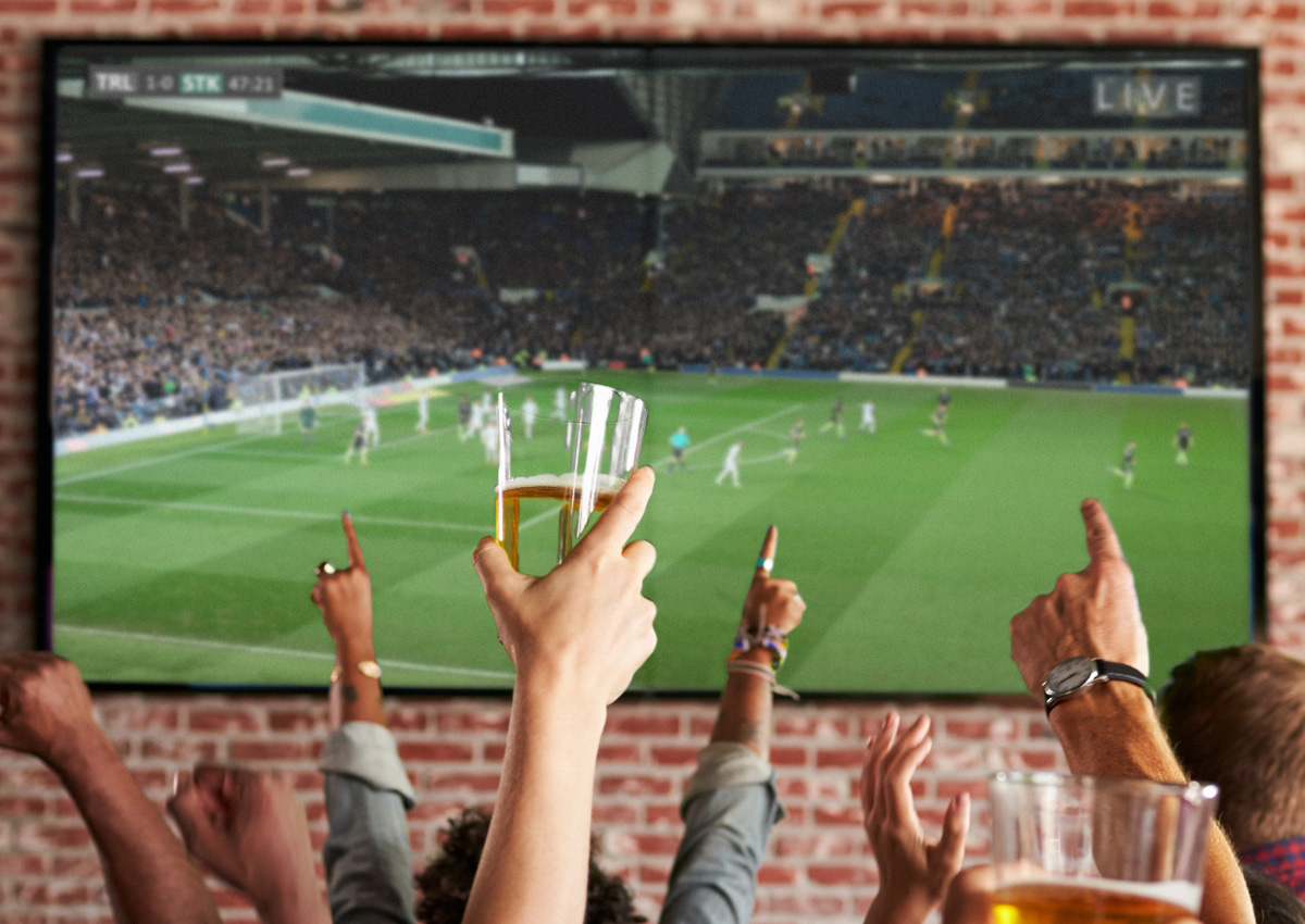 Leinwand auf dem ein Fußballspiel übertragen wirdin einer Gaststätte mit jubelnden Fans