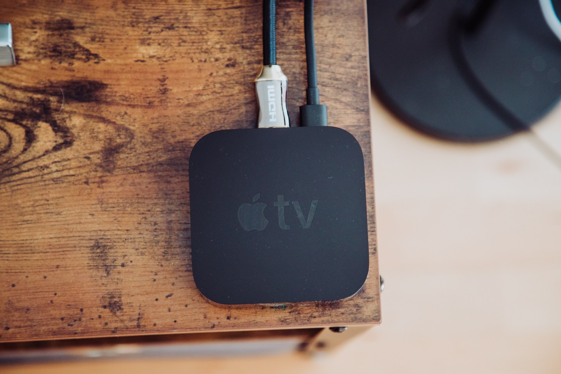 Ein Apple TV-Gerät liegt auf einer hölzernen Oberfläche, verbunden mit einem HDMI-Kabel und einem Stromkabel.