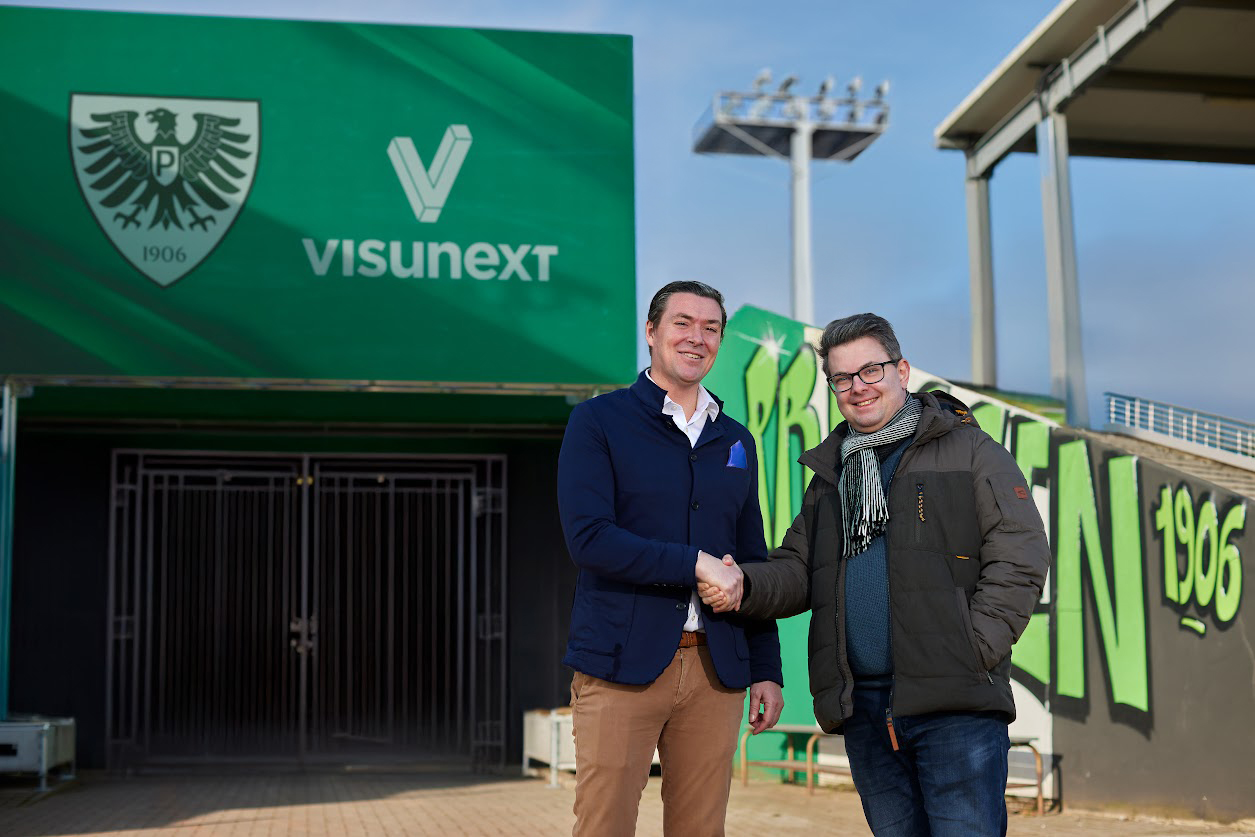 Dr Axel Niclas (Sr. Director Sales & Business Development, visunext SE) und Dr Marcus Sass (Geschäftsführer Finanzen, Stadion & Organisation, SC Preussen Münster) beim Handschlag vor der installierten LED-Wall im Stadion von Preußen Münster mit visunext-L