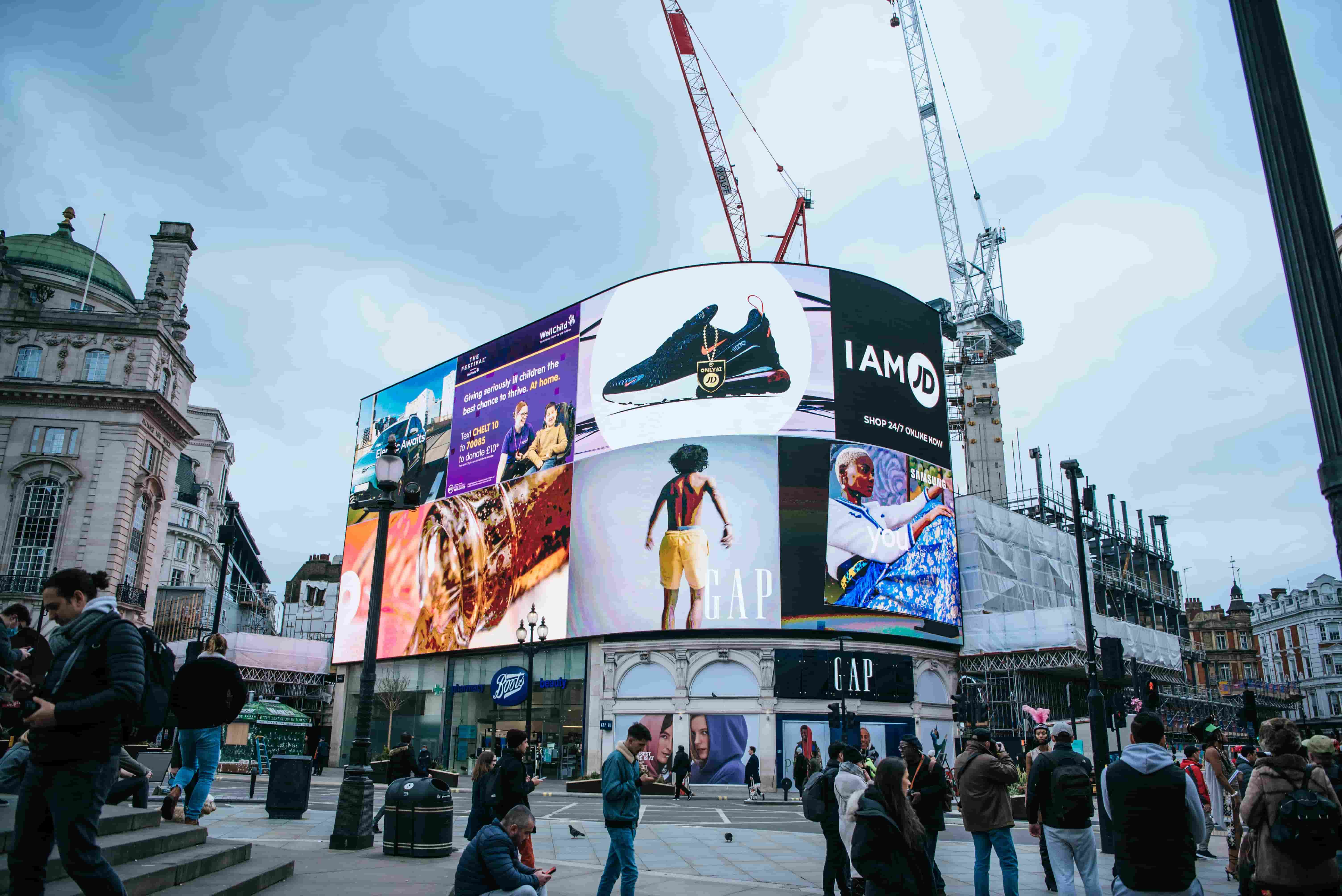 In der Mitte des Bildes sieht man ein großes Gebäude, welches mit videowalls ausgestattet ist. Auf iesen ist Werbung zu sehen