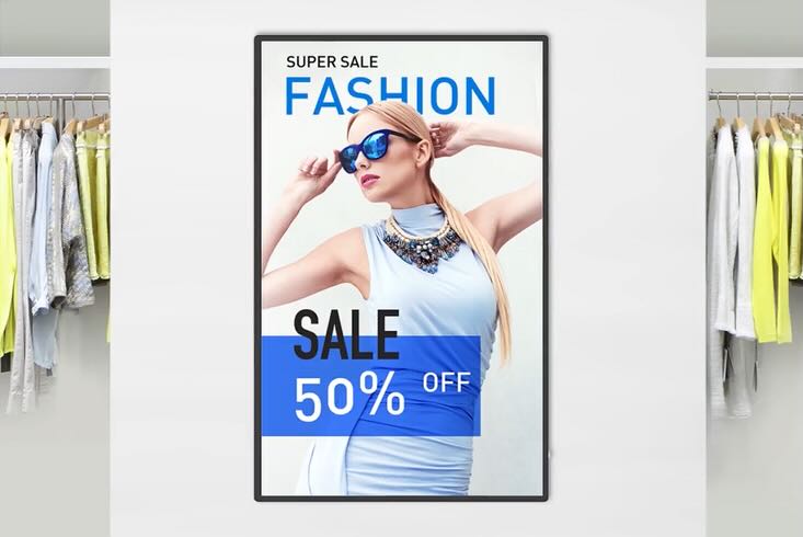  Ein großes vertikales Digital Signage Display zeigt ein Mode-Werbeplakat. Auf dem Plakat ist eine schlanke blonde Frau mit Sonnenbrille und einer Statement-Halskette abgebildet. Der Text auf dem Plakat lautet "SUPER SALE FASHION" oben und "SALE 50% OFF" 