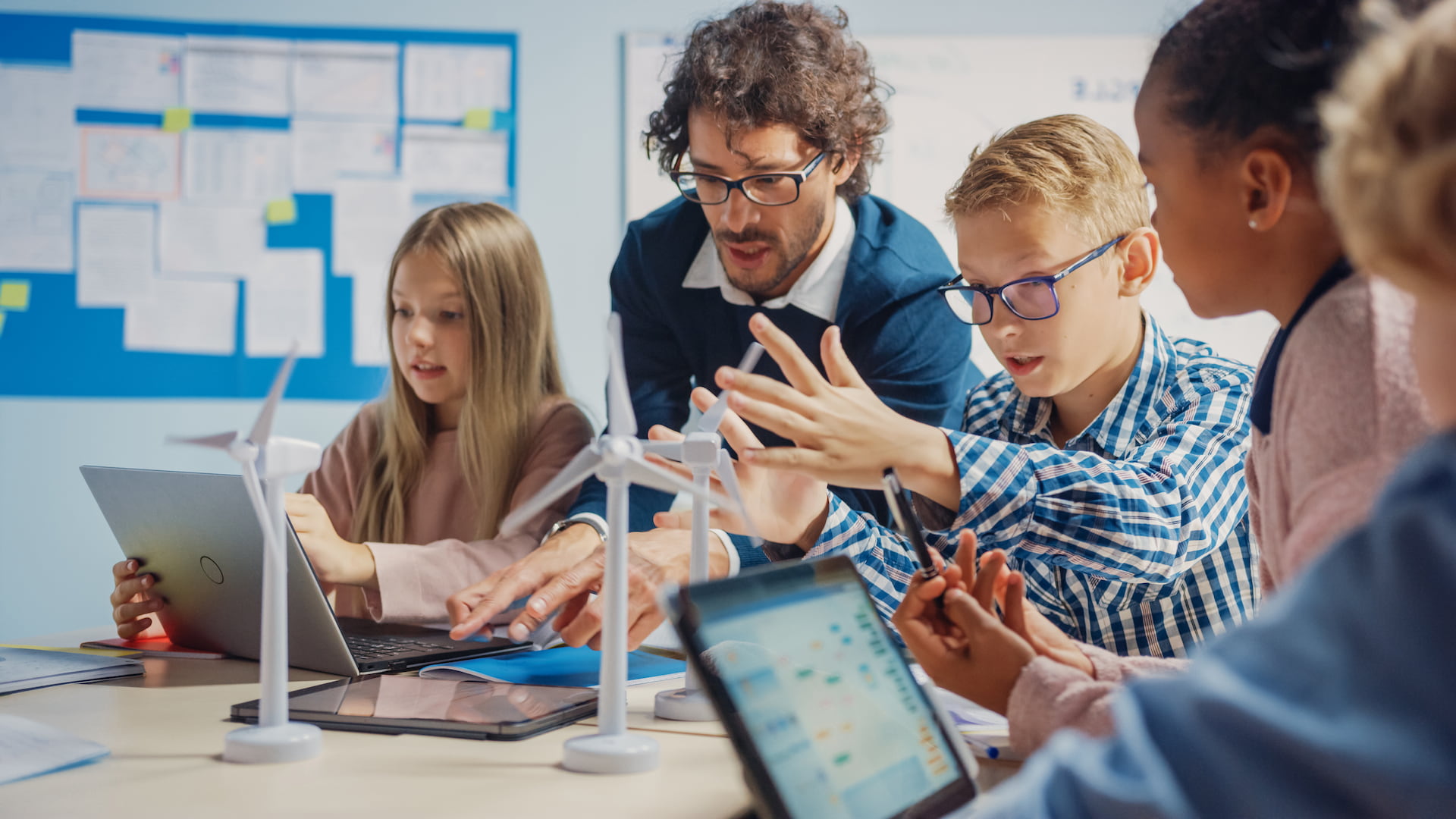 Auf dem Bild ist ein Lehrer mit Kindern zu sehen, die gemeinsam interaktiv mit Tablets arbeiten.