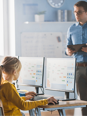 Klassenraum mit Leher und Schülern die an Computer arbeiten